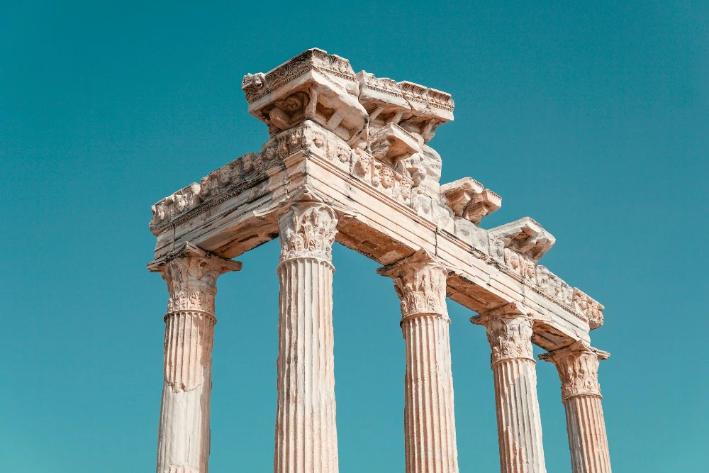 Image of ancient greek or roman structure consisting of columns, set against a sky blue background.
